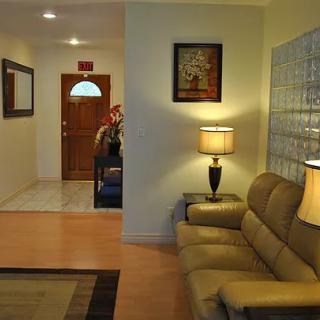 A cozy living room with a leather sofa and lamp, leading to a hallway adorned with artwork.