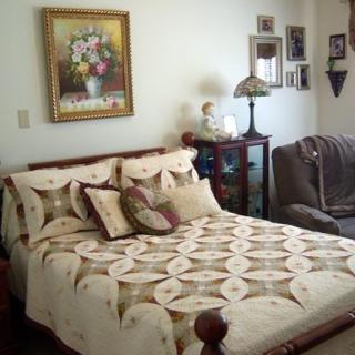 A cozy bedroom featuring a decorative quilt on the bed, floral painting on the wall, and classic furniture.