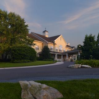 A serene residential building with a welcoming pathway surrounded by lush greenery during sunset.