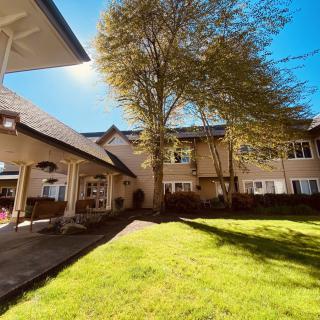 A scenic view of a building with a lush green lawn and a large tree under the bright sunshine.