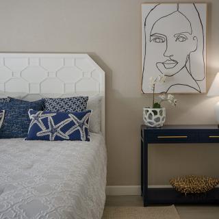 A modern bedroom with a white headboard, decorative pillows, and a minimalist artwork on the wall.