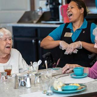 A caregiver shares a joyful moment with seniors during a meal at a community center.
