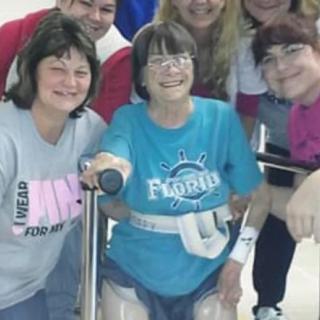A group of people smiling together, centered around an individual using a mobility aid.