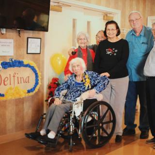 A group of people celebrating a birthday with an elderly woman in a wheelchair.