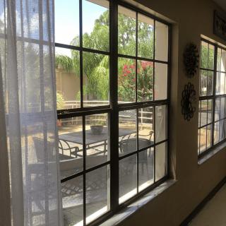 A sunny view through large windows with curtains, revealing an outdoor seating area and garden.