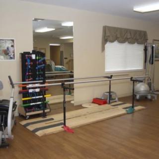 A rehabilitation room with parallel bars, a mirror, and various gym equipment.