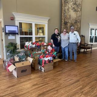 A group of three people standing next to a collection of gift boxes in an indoor setting.