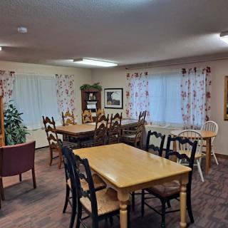 A cozy dining area with wooden tables and chairs, decorated with floral curtains and warm lighting.