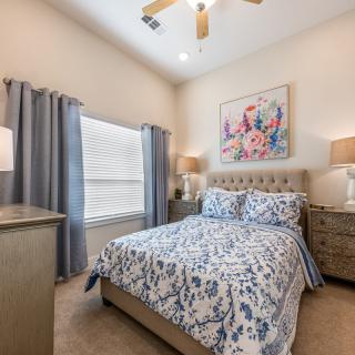 A beautifully decorated bedroom featuring a bed with floral bedding, two nightstands with lamps, and a large window with curtains.