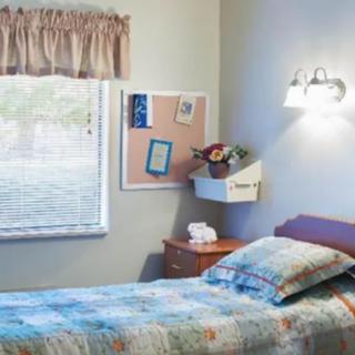 A cozy bedroom with a single bed, a bulletin board on the wall, and a small flower vase on the bedside table.