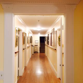 A well-lit hallway with wooden floors and paintings displayed on the walls.
