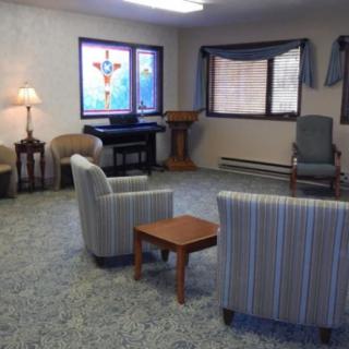 A small chapel room with chairs, a table, and stained glass windows.