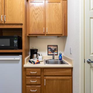 A compact kitchenette with wooden cabinets, a microwave, mini fridge, and sink.