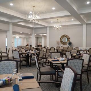 An elegantly decorated dining room with multiple tables and chairs, featuring chandeliers and a mirror on the wall.