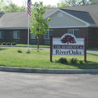 A residential building featuring a sign for RiverOaks, with a lawn and an American flag in front.
