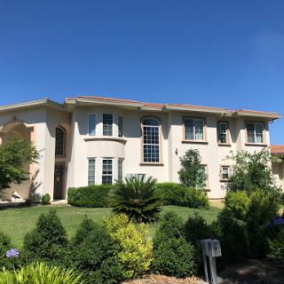 A beautiful two-story house surrounded by lush greenery under a clear blue sky.