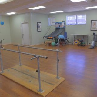 A rehabilitation therapy room equipped with parallel bars and various exercise equipment.