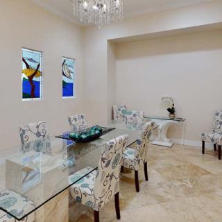 A modern dining room with a glass table and decorative chairs, highlighted by stained glass windows and a chandelier.
