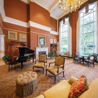 A luxurious and elegantly designed living room featuring a grand piano, high ceilings, and large windows.