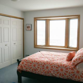 A cozy bedroom with a large window, featuring a bed with floral bedding and a spacious closet.