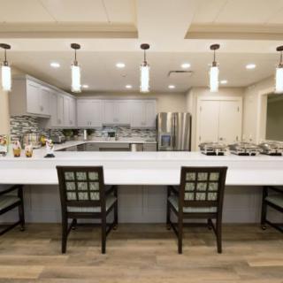 A modern kitchen with a large white countertop, bar stools, pendant lighting, and stainless steel appliances.