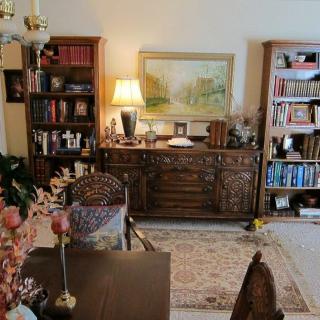 A cozy living room with bookshelves, a lamp, artwork, and a rug.