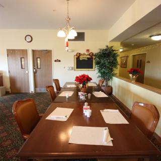 A neatly arranged dining room with a long wooden table, surrounded by chairs and set with placemats, featuring a centerpiece of flowers under warm lighting.