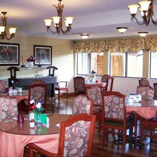 A cozy restaurant dining area with multiple tables and chairs, decorative chandeliers hanging from the ceiling, and large windows providing natural light.
