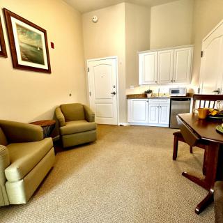 A cozy living room with a kitchenette, featuring comfortable seating and tasteful artwork.