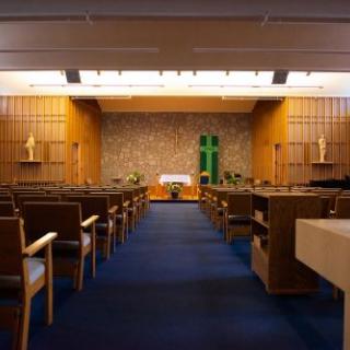An empty chapel interior with rows of pews facing an altar.