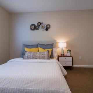 A modern and cozy bedroom with a neatly made bed, decorative pillows, and a bedside table with a lamp.