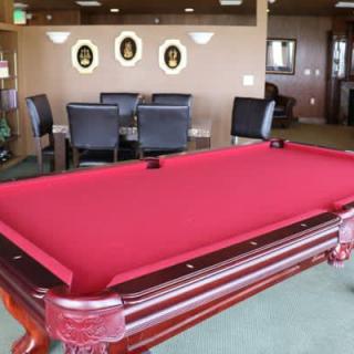 A billiards room featuring a red-felt pool table and a seating area in the background.