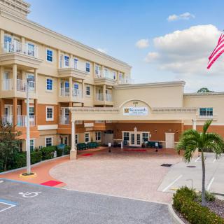 A hotel entrance with an American flag and palm trees in the parking area.