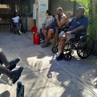 A group of individuals sitting outside a care facility, some in wheelchairs, enjoying the sunlight.