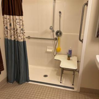 An accessible bathroom shower with a seat and grab bars, designed for ease of use.