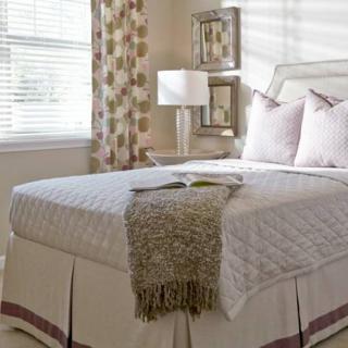 A neatly arranged bedroom featuring a made bed with pillows and a throw, alongside a lamp by the window.