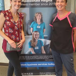 Two women standing next to a healthcare clinic poster.