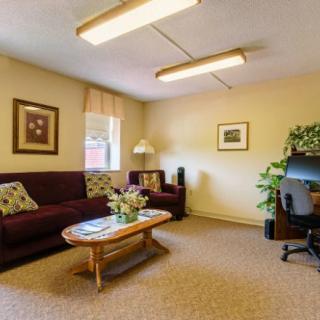 A cozy living room with a sofa, coffee table, artwork on the walls, and a computer desk with an indoor plant.