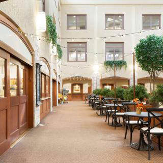A serene indoor courtyard featuring a seating area with tables and chairs, surrounded by plants and ambient lighting.