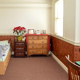 A cozy bedroom with a bed, dresser, and window, featuring a plant and wooden furniture.