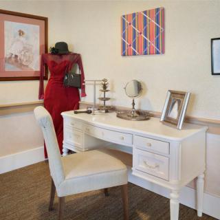 A cozy home office setup featuring a white desk with a mirror, framed art pieces on the wall, and a woman in red observing the decor.