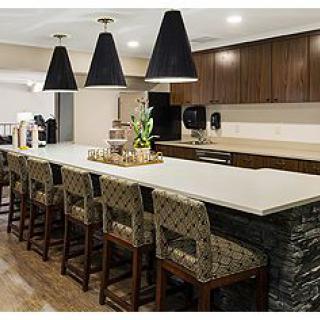 A modern kitchen featuring a long countertop with bar stools, pendant lighting, and dark wood cabinetry.