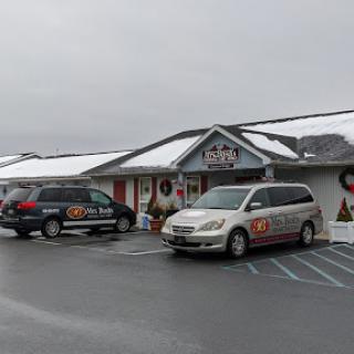 A snowy scene featuring a building with holiday decorations and parked vehicles.