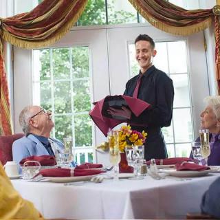 A waiter serves guests at a restaurant table with a formal setting.