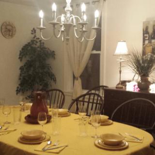 A cozy dining room with a neatly set table, featuring a yellow tablecloth and ambient lighting from a chandelier.