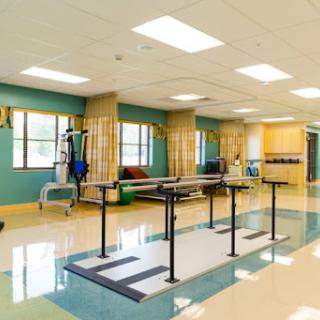 A bright and spacious physical therapy room equipped with parallel bars and various rehabilitation tools.