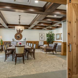 A well-furnished dining room with a large table and chairs, featuring wooden ceiling beams and elegant decor.