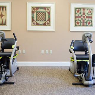 A gym room featuring two stationary bikes and framed artwork on the walls.