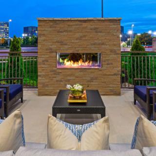 A cozy outdoor patio with a modern fireplace and comfortable seating, set against an evening cityscape.