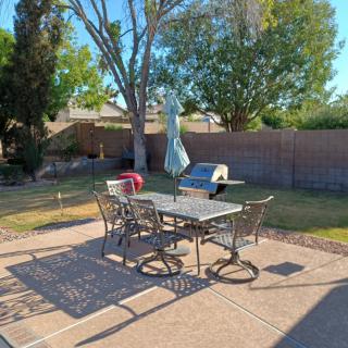 A sunny backyard with a patio table and chairs, surrounded by trees and a brick fence.